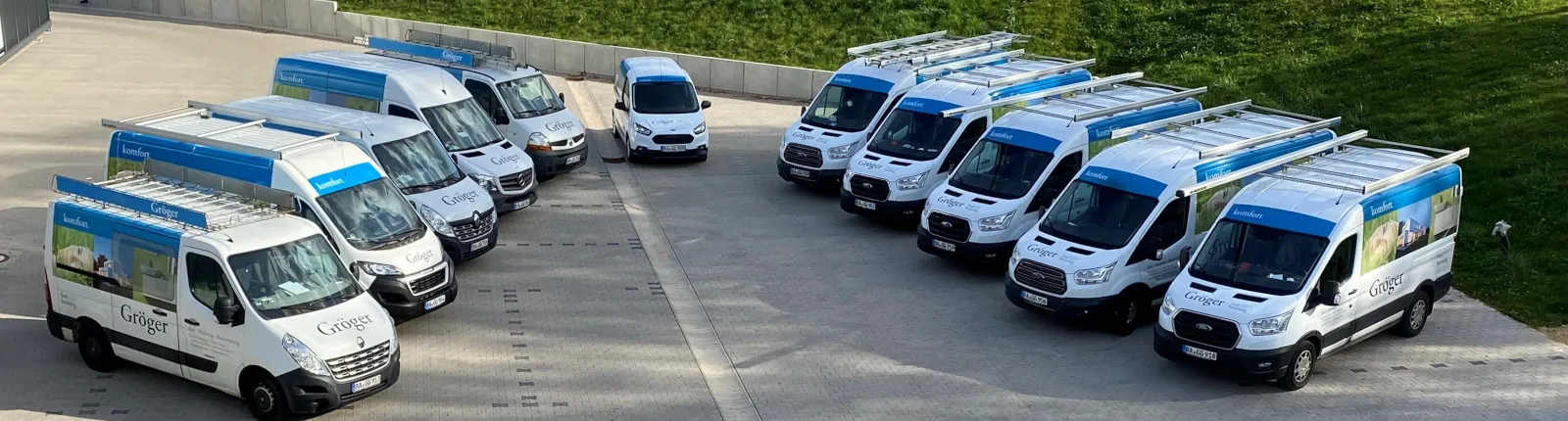 Zehn Transporter des Handwerksbetriebs Gröger bad und heizung sind in zwei Reihen auf einem Parkplatz in V-Formation aufgestellt.